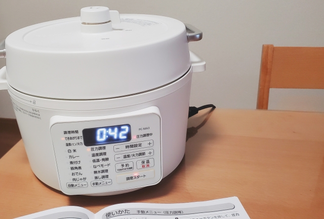 木のテーブルの上に電機圧力鍋が置かれている画像